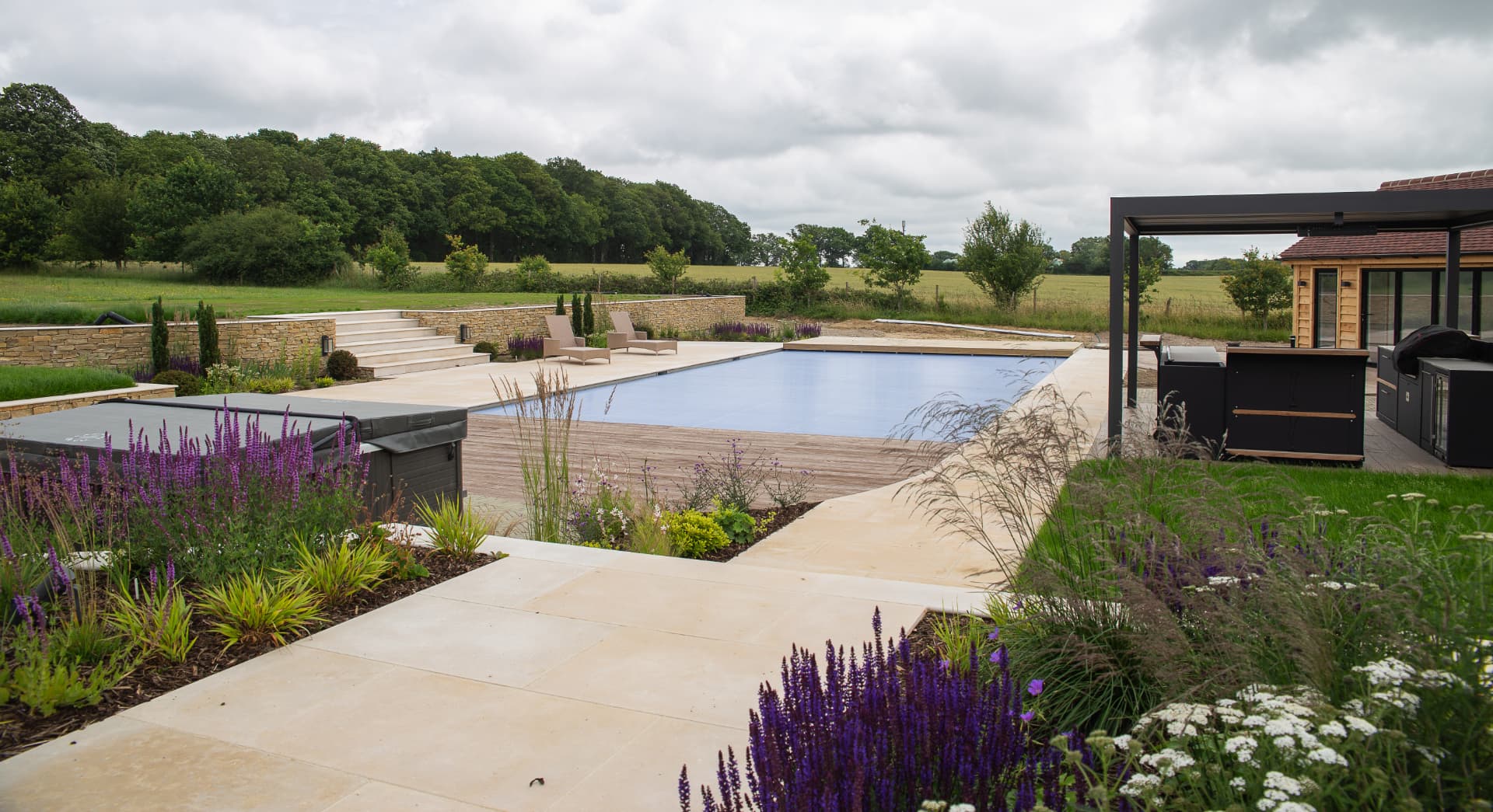 Luxury pool terrace with natural stone paving, outdoor kitchen, pergola, hot tub and planted borders